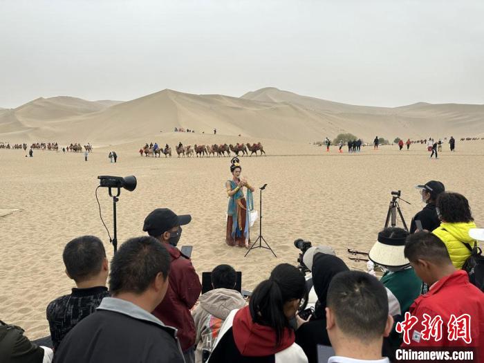 圖為2023年4月底，敦煌大漠“逐舞者”奧楠在鳴沙山月牙泉景區(qū)視頻直播，吸引游人圍觀?！●T志軍 攝